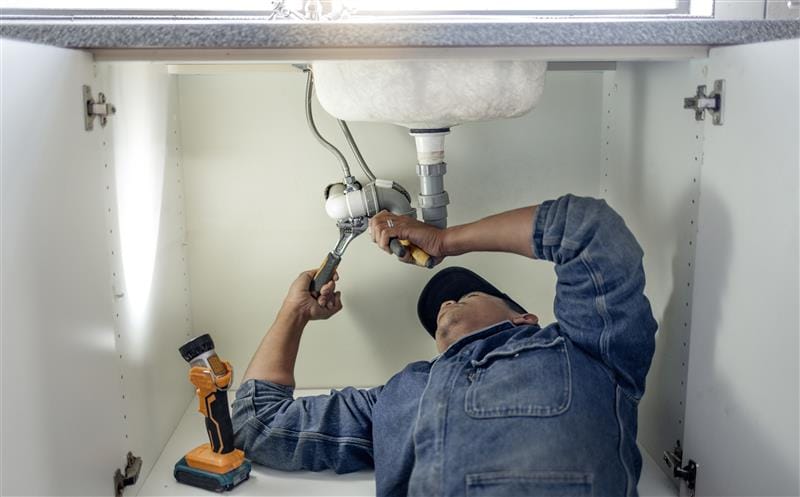 Plumber repairing pipes beneath a bathroom sink in Margate