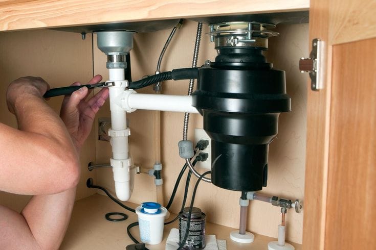 Plumber installing a garbage disposal beneath a kitchen sink in Margate