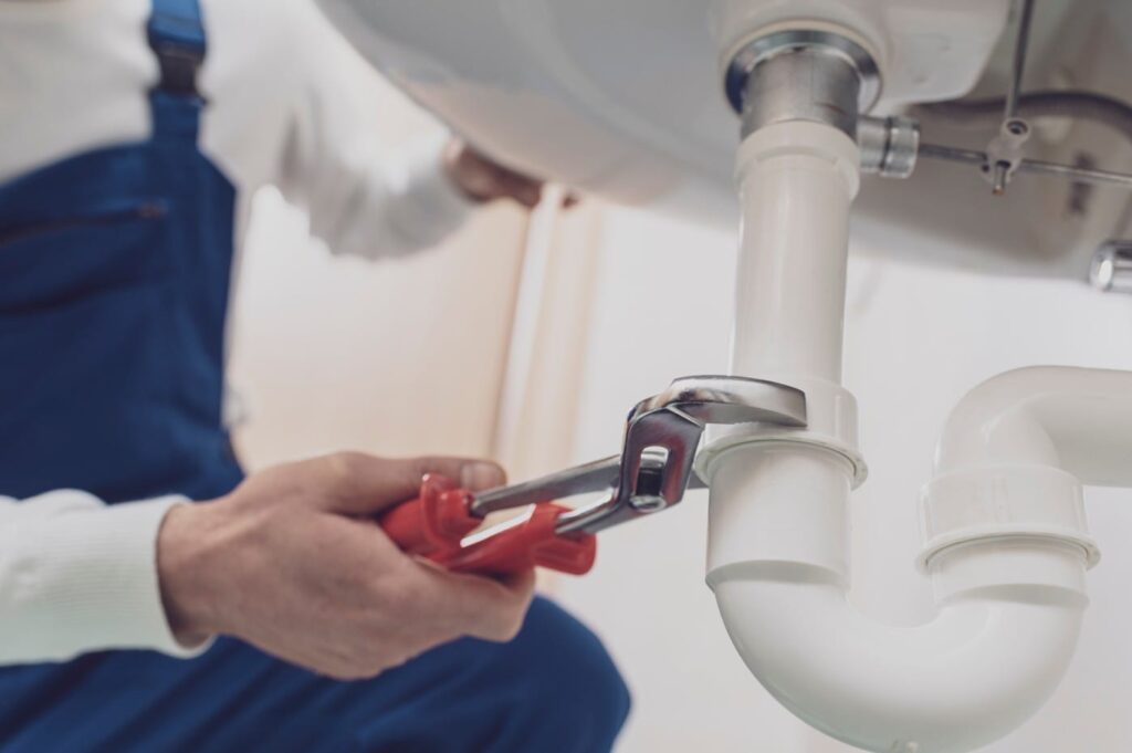 Plumber repairing a white drain pipe beneath a sink in Margate