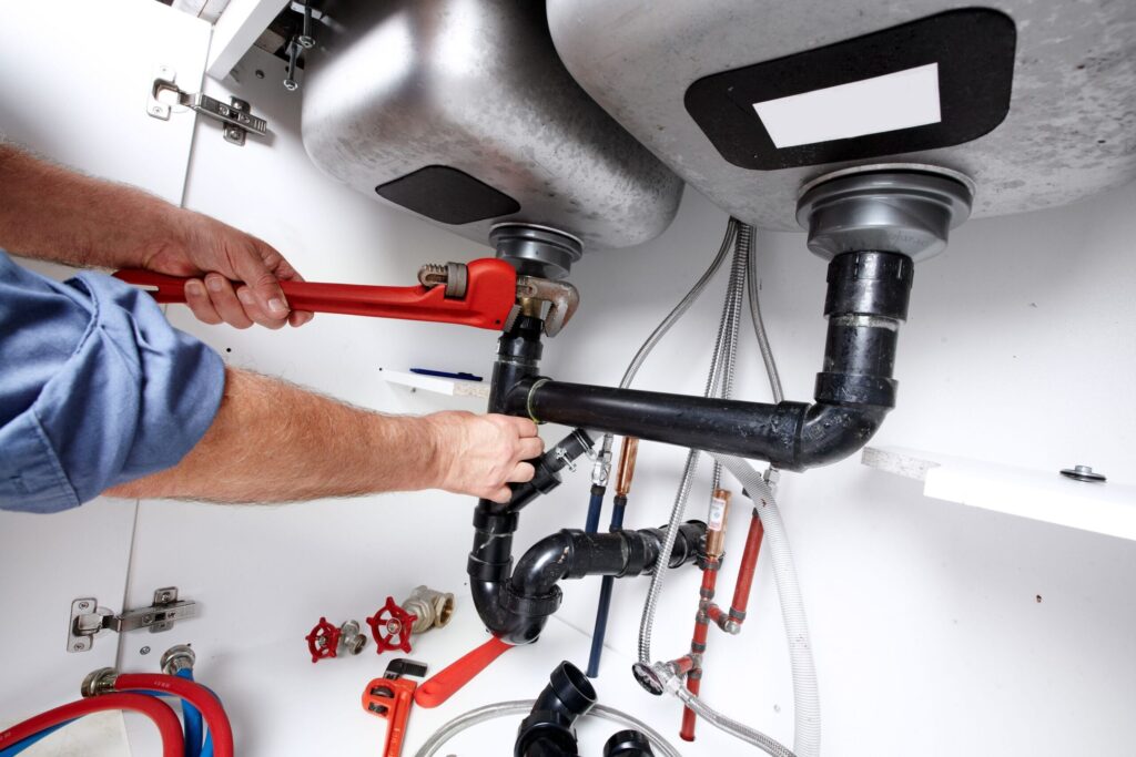 Plumber repairing drain pipes beneath a kitchen sink in Margate