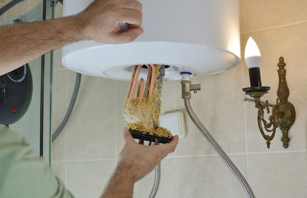 Technician removing mineral buildup from a water heater in Margate